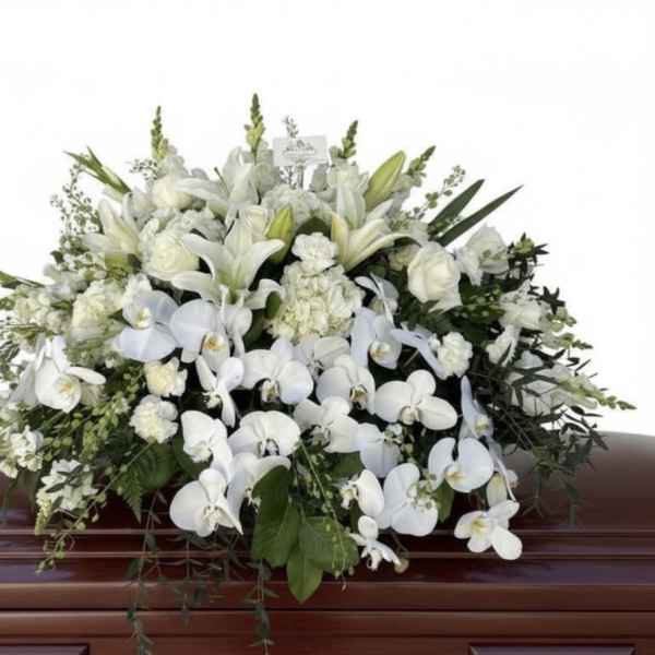 Large white casket spray of lilies, roses, carnations, and orchids on a wooden casket.