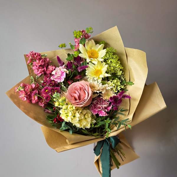 Hand-tied bouquet of pink, yellow, and purple flowers in kraft paper