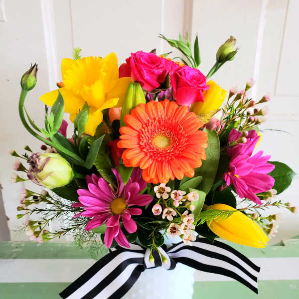 Bright mixed bouquet in a white vase with a black-and-white ribbon