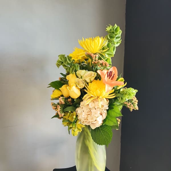 Yellow mixed flower arrangement in a tall glass vase