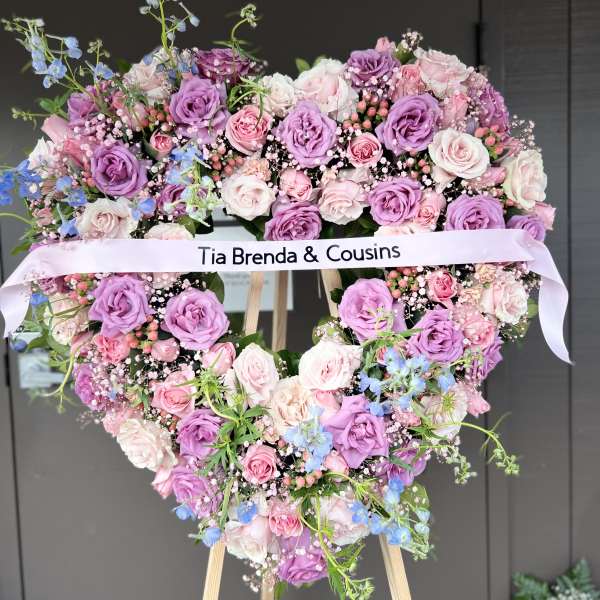 Heart-shaped floral wreath of pink and purple roses with a ribbon banner