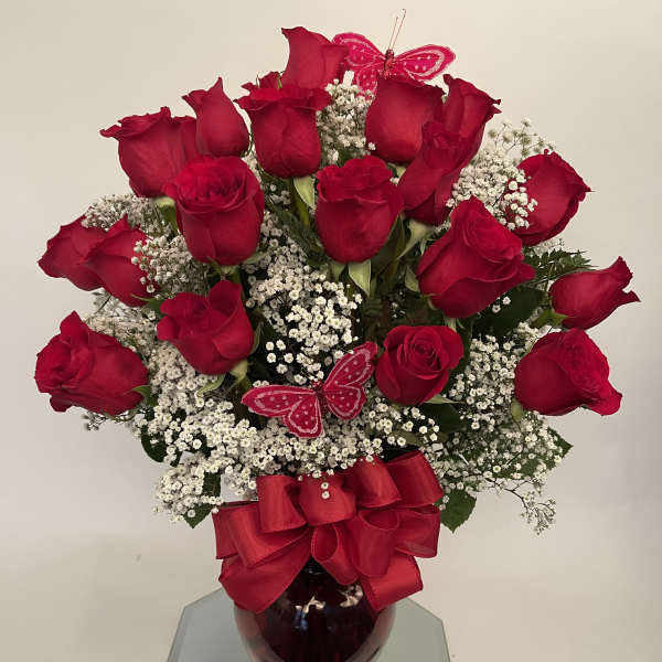 Red roses with baby's breath in a glass vase, accented by red bows and butterfly picks
