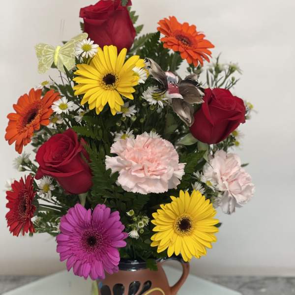 Mixed bouquet of roses, gerbera daisies, and carnations in a decorative mug