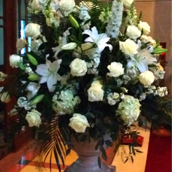 Large white floral arrangement in a pedestal vase with lilies and roses