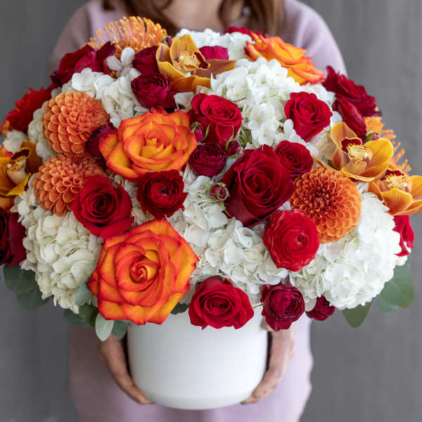 Large bouquet of red, orange, and white flowers in a white vase