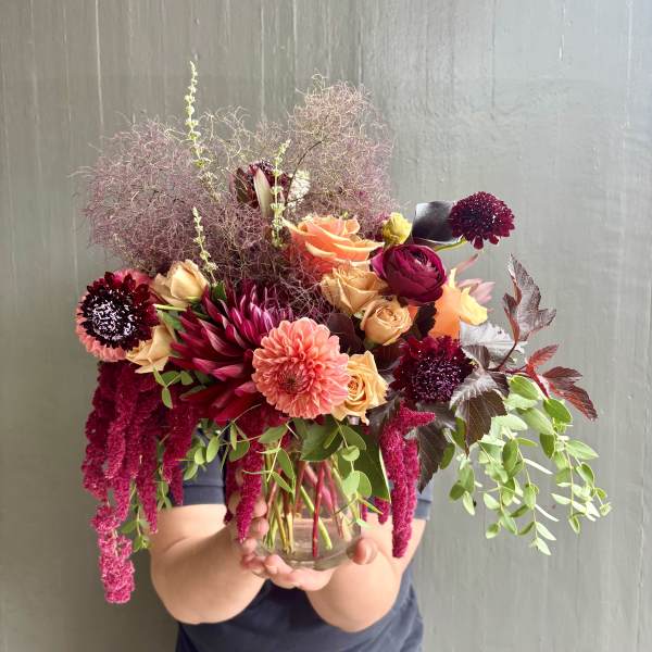 Mixed bouquet in a clear glass vase with peach, burgundy, and pink blooms