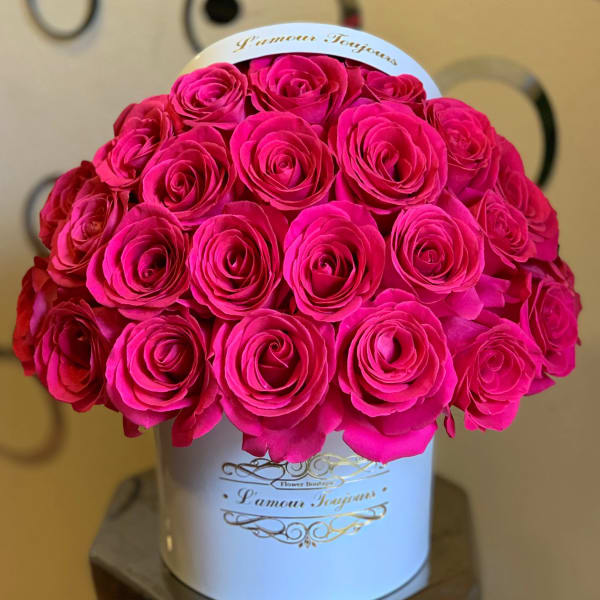 Round bouquet of bright pink roses arranged tightly in a white hatbox-style container.