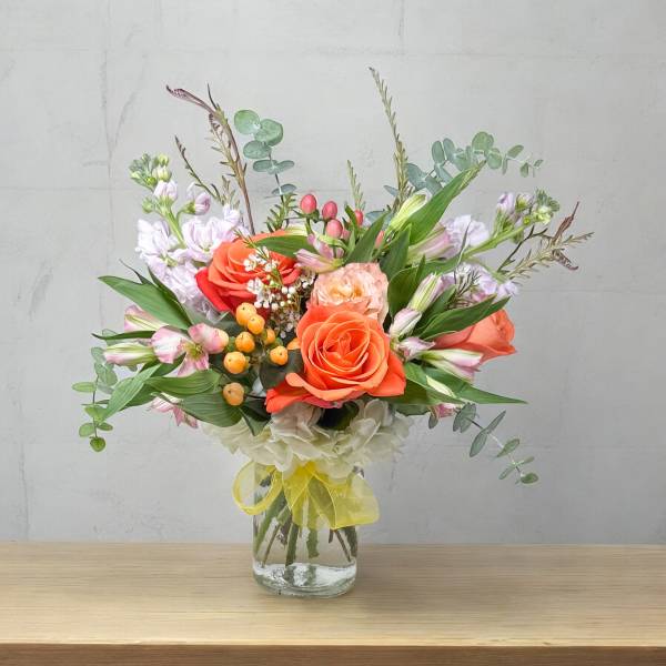 Bouquet of orange roses and pastel flowers in a glass vase with a yellow ribbon