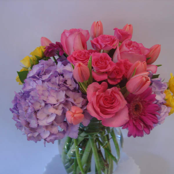 Mixed bouquet of pink roses, tulips, hydrangeas, and a gerbera daisy in a glass vase