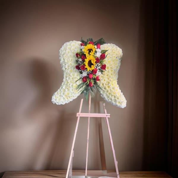 Heart-shaped floral standing spray with white flowers, red roses, and sunflowers on an easel