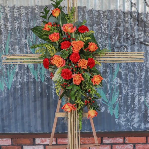 Tall floral standing arrangement with orange roses and red carnations on an easel