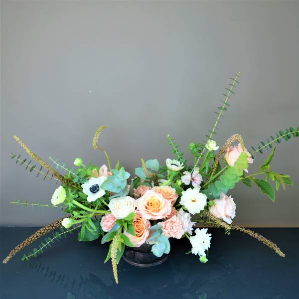 Low floral arrangement with peach and white roses in a black container