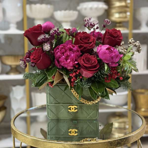 Red and pink rose arrangement in a green quilted handbag-style container