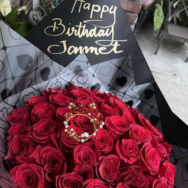 Bouquet of red roses wrapped in black heart-patterned paper with a birthday tag