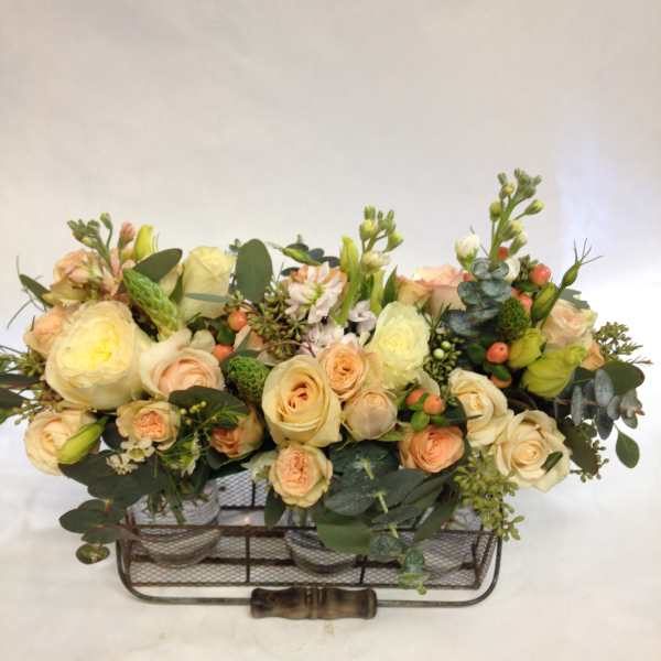 Low floral arrangement of cream and peach roses in a metal basket