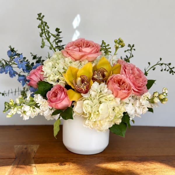 Pink roses, white hydrangeas, and yellow orchids in a white vase