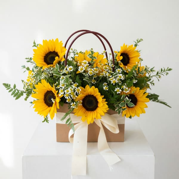 Basket arrangement of sunflowers and small white daisies with a ribbon bow