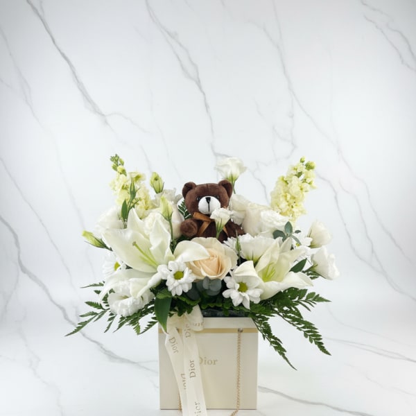 White floral arrangement with a small teddy bear in a Dior gift box