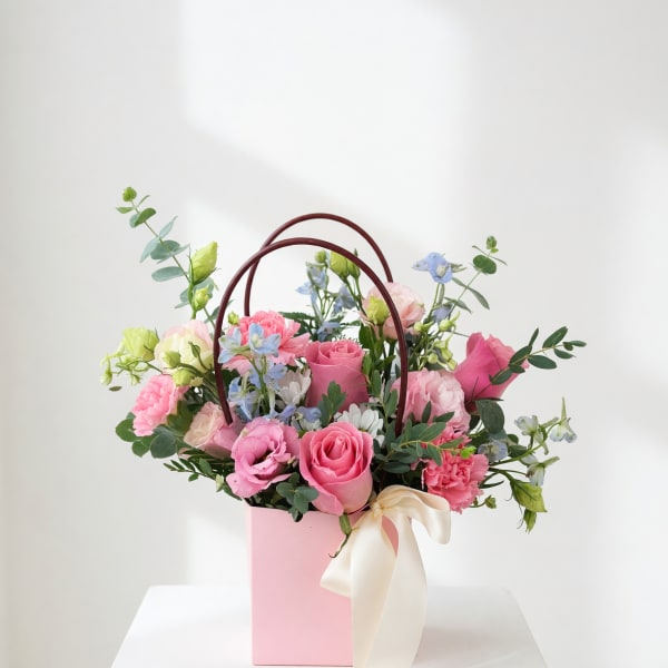 Pink and blue mixed flower arrangement in a pink gift box with ribbon handles