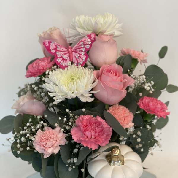 Pink and white flower arrangement in a white pumpkin vase with a butterfly decoration