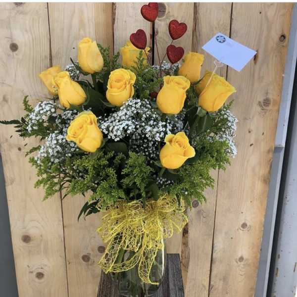 Yellow roses in a clear vase with baby's breath and a red heart pick