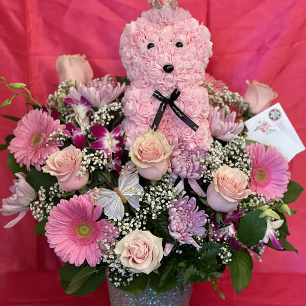 Pink teddy bear in a flower arrangement with roses and gerbera daisies