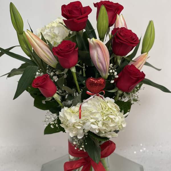 Red roses and white hydrangeas in a glass vase with a red ribbon