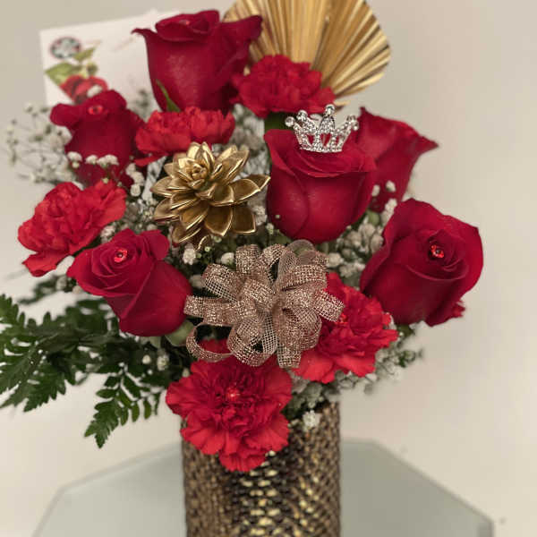 Red roses and carnations in a gold vase with decorative bows and a crown