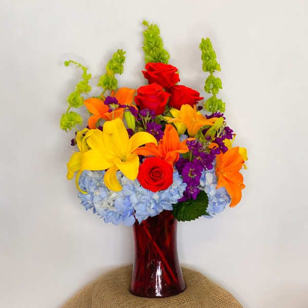 Colorful bouquet of roses, lilies, and hydrangeas in a red glass vase
