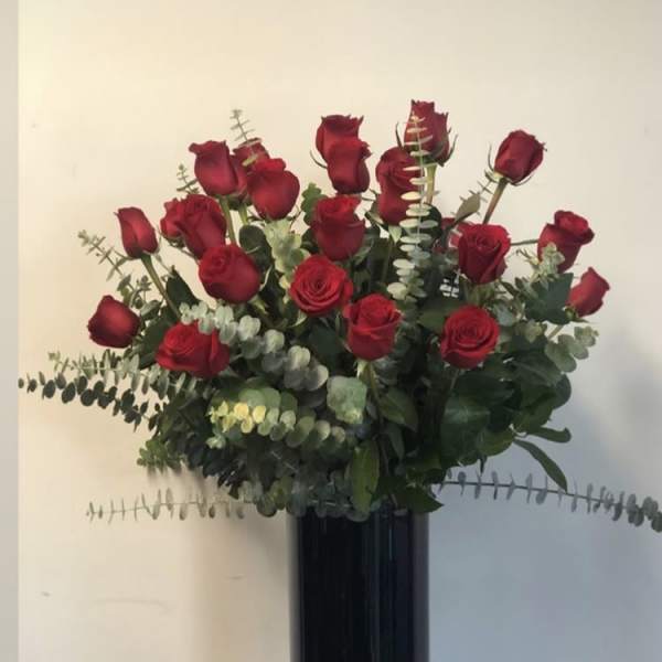 Red roses arranged in a tall black vase with eucalyptus