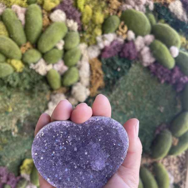 Hand holding a purple heart-shaped crystal against a floral wall