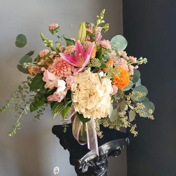 Mixed bouquet with pink lilies, cream hydrangea, and orange blooms in a glass vase