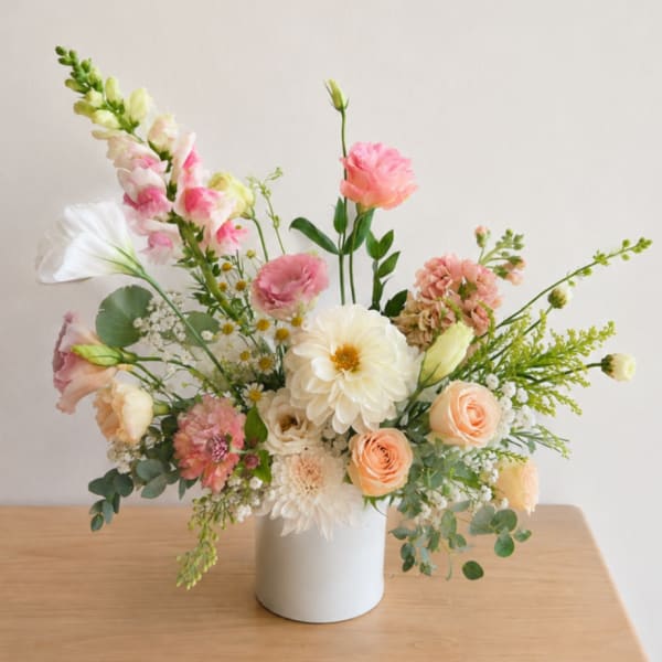 Pastel floral arrangement in a white vase with pink and cream blooms