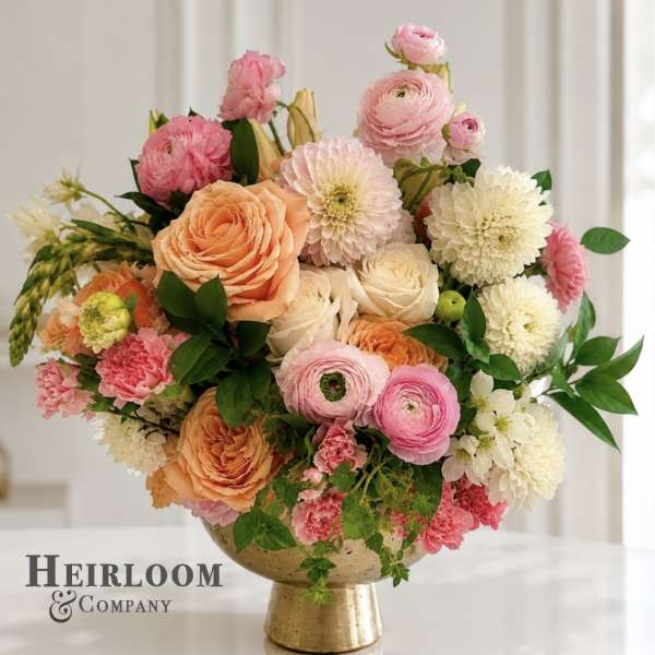 Pink, peach, and white flowers arranged in a gold pedestal vase