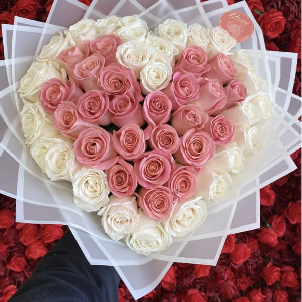 Heart-shaped bouquet of pink and white roses wrapped in translucent paper