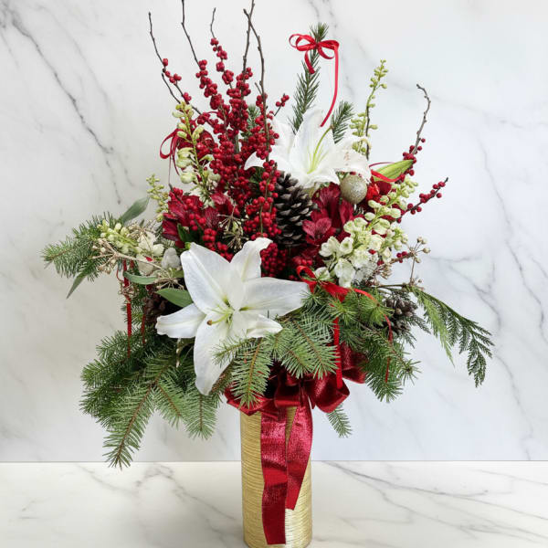 Holiday arrangement with white lilies, red berries, and pine in a gold vase