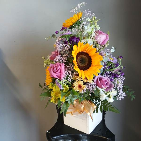 Mixed bouquet with sunflowers, pink roses, and purple flowers in a white box