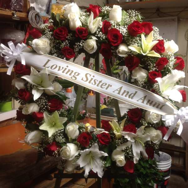 Heart-shaped wreath of red and white roses with lilies and a memorial ribbon