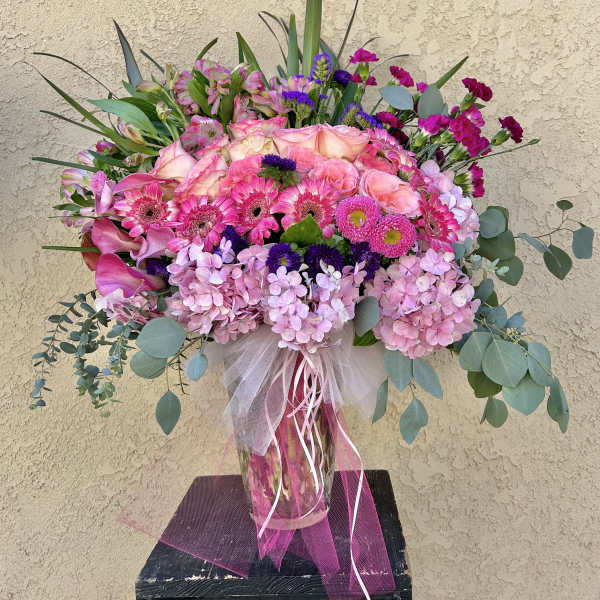 Large pink and purple floral arrangement in a glass vase with ribbon