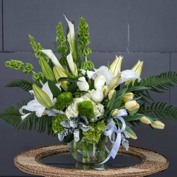 White lilies and green blooms arranged in a glass vase with a ribbon