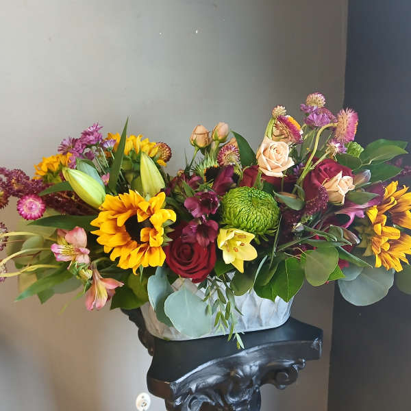 Mixed bouquet of sunflowers, roses, and lilies in a white container