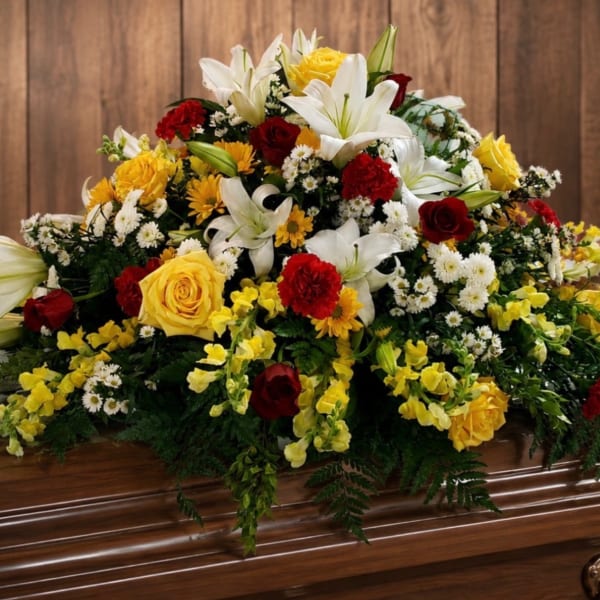 Large floral casket spray with white lilies, yellow roses, and red carnations