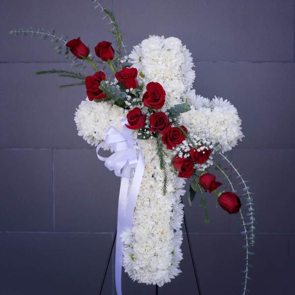 White floral cross with red roses on a stand