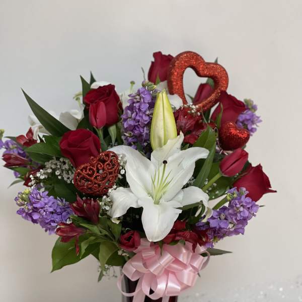 Bouquet of red roses, white lilies, and purple flowers in a vase with pink ribbon
