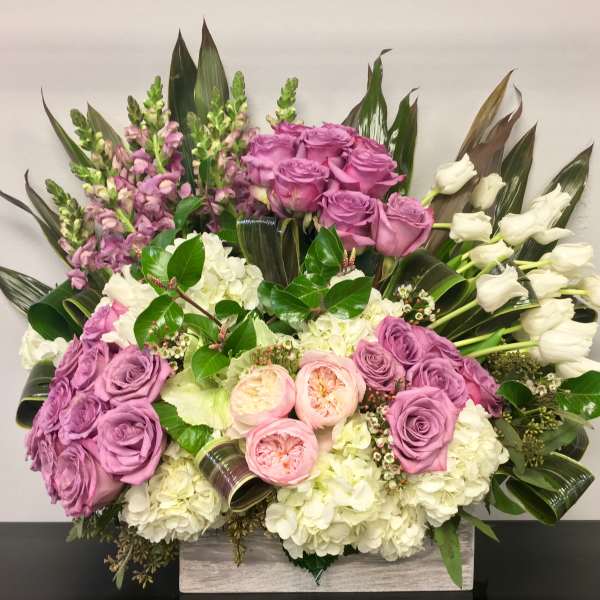 Low rectangular arrangement with lavender roses, white hydrangeas, pink roses, and white tulips.