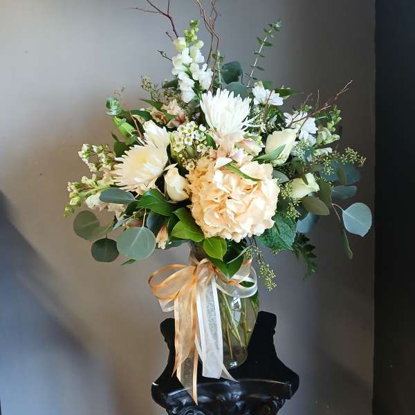 Cream and white bouquet in a clear glass vase with ribbon