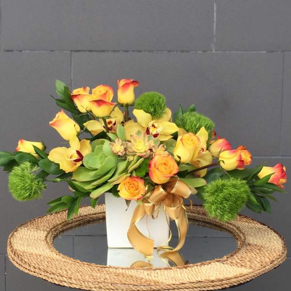 Yellow and orange roses with green accents in a white vase