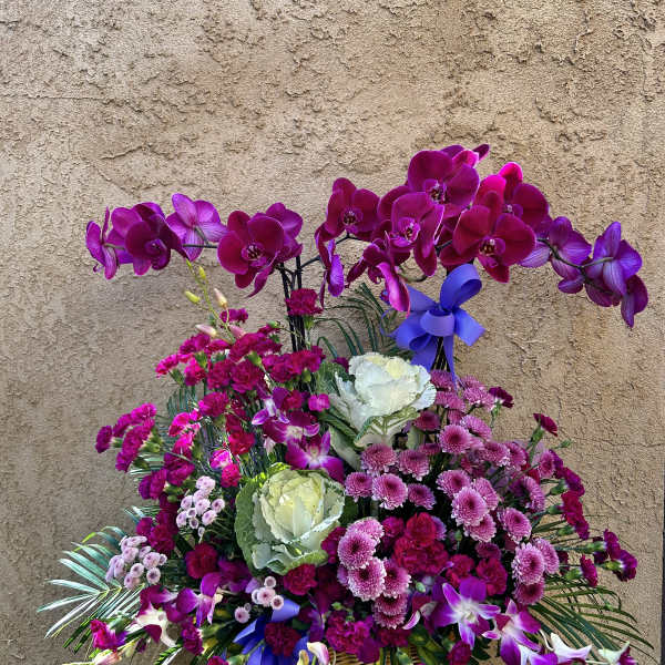 Basket arrangement of purple orchids, carnations, and mums with blue ribbons