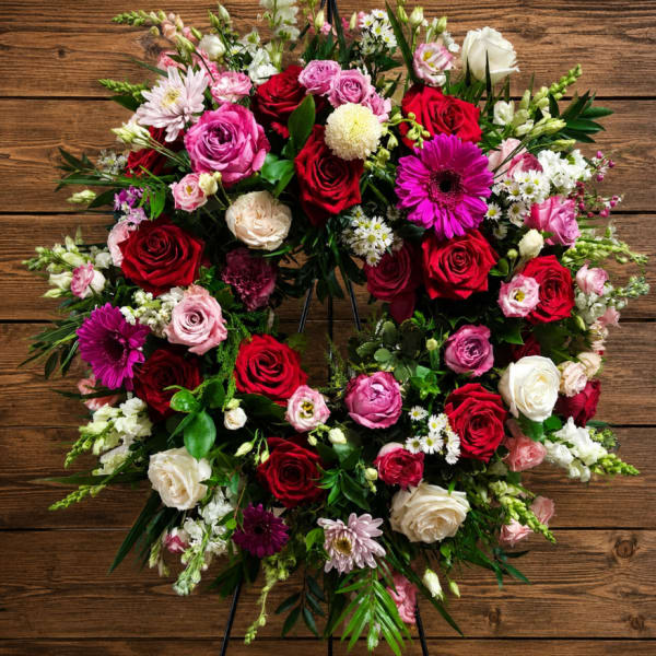 Heart-shaped floral wreath with red, pink, and white blooms on a stand