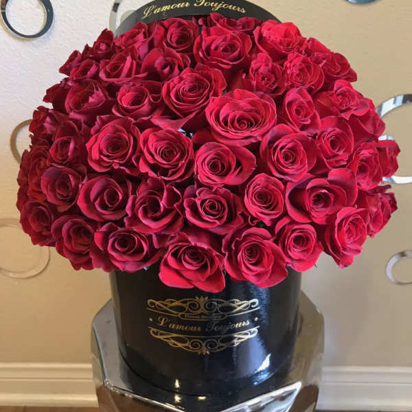 Large dome of red roses arranged in a round black hatbox with gold lettering.